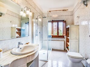 Un baño moderno con un lavabo grande, un inodoro, cabina de ducha y una ventana con vistas a la vegetación.