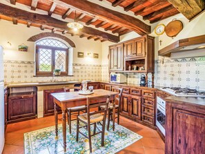 Una cuina amb armaris de fusta, un frontó de rajola, una taula de dinar amb caires i una finestra amb vistes.