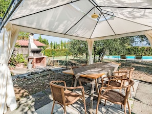 Eine Terrasse im Freien mit Tisch und Stühlen, einem Grill und einem Pool im Hintergrund.