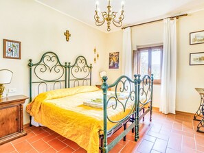 Una camera da letto con un letto, un lampadario, una finestra con tende e opere d'arte alle pareti.
