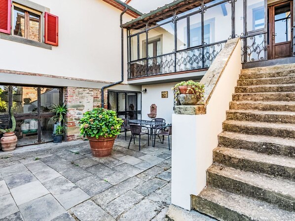 Un cortile con pavimento in pietra, una grande pianta in vaso, mobili da esterno e una scala che conduce a un livello superiore.