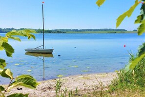 En stilla sjö med en segelbåt som ligger ankrad nära stranden, omgiven av grönska och en klar himmel.