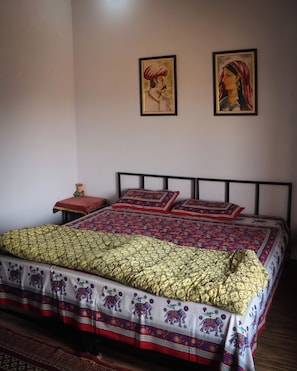 Una cama con una colcha estampada y almohadas, una mesita de noche con un objeto decorativo, y dos cuadros en la pared.