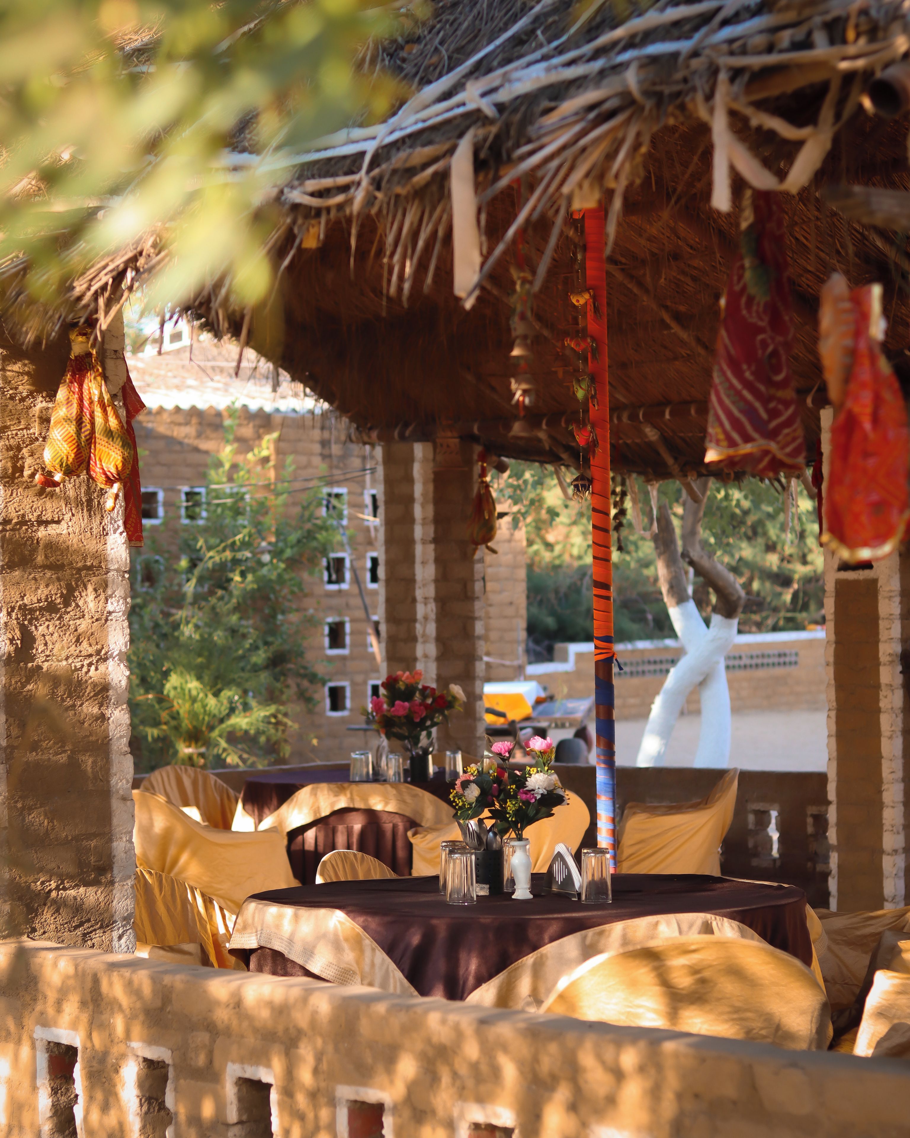 Un área de comedor al aire libre con mesas dispuestas para dos, cubiertas con manteles amarillos y un techo de paja.