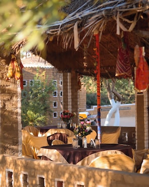 Un área de comedor al aire libre con mesas dispuestas para dos, cubiertas con manteles amarillos y un techo de paja.