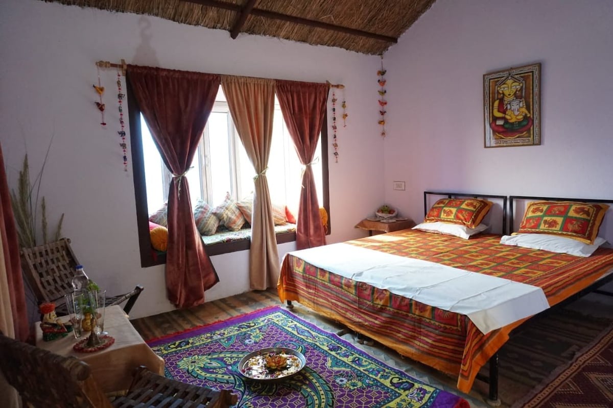 Una habitación con dos camas, una ventana con cortinas, un adorno en la pared y un tapete tradicional en el suelo.