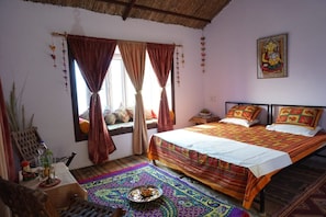 Una habitación con dos camas, una ventana con cortinas, un adorno en la pared y un tapete tradicional en el suelo.