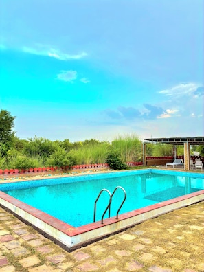 Una piscina con borde rojo, una zona de estar cubierta y un césped con valla.
