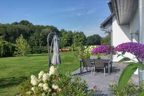 A patio area with a table and chairs, surrounded by a garden with various plants and flowers. - Holiday apartment with 2 bedrooms (Heidesee)