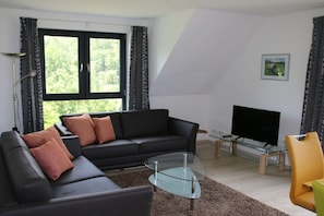 A modern living room with a black sofa, glass coffee table, and a flat-screen TV. - Holiday apartment with 2 bedrooms (Heidesee)