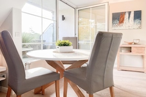 A modern dining area with a round table, two grey upholstered chairs, and a potted plant. - Holiday apartment with 1 bedroom (Timmendorfer Strand)