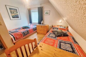 Ein Zimmer mit zwei Betten, einem Holzschrank, einem Stuhl und einem Fenster mit Vorhängen.