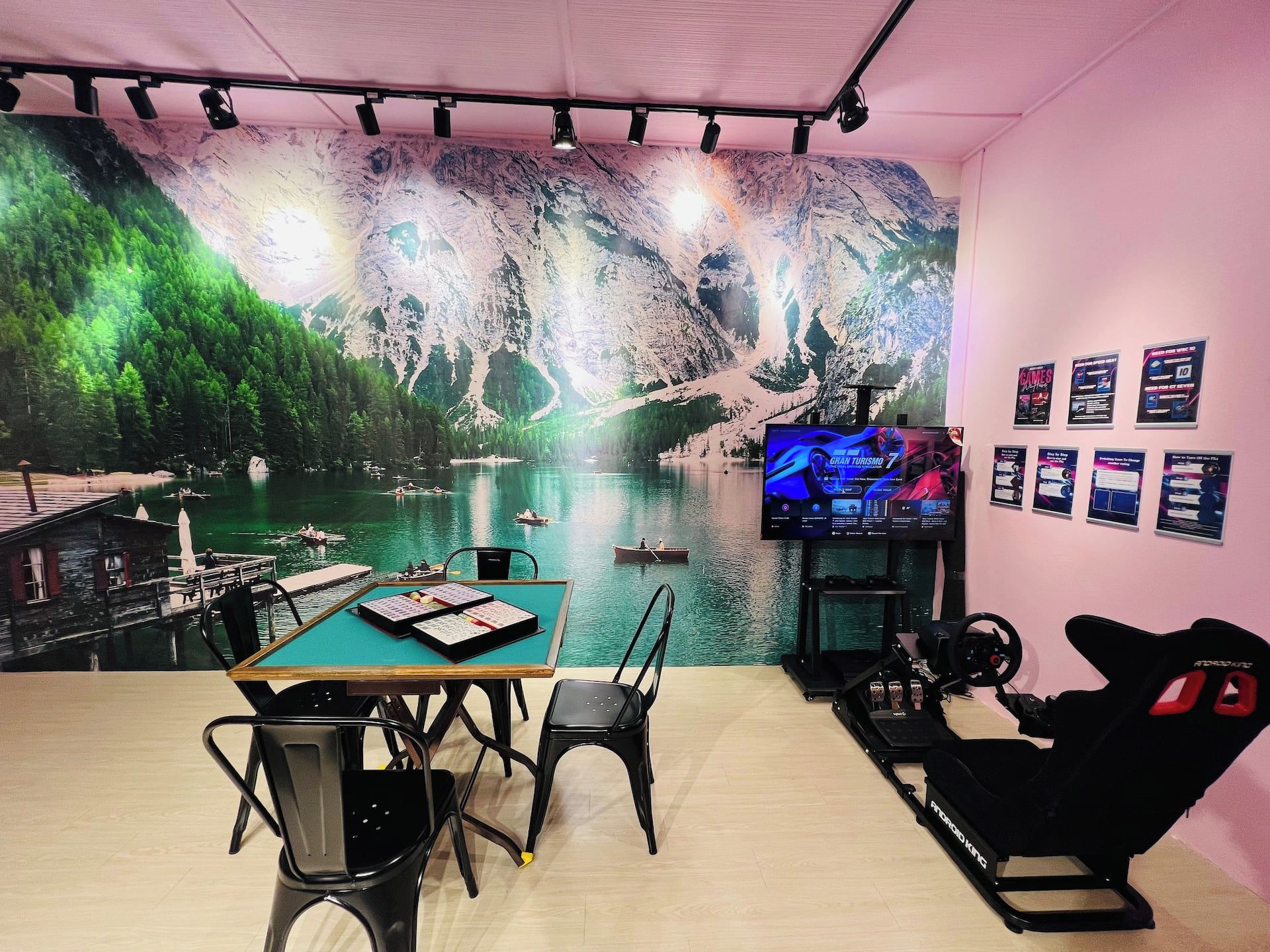 Una habitación con un mural grande de un paisaje montañoso, una estación de juego con monitor, sillas y un volante de carreras.