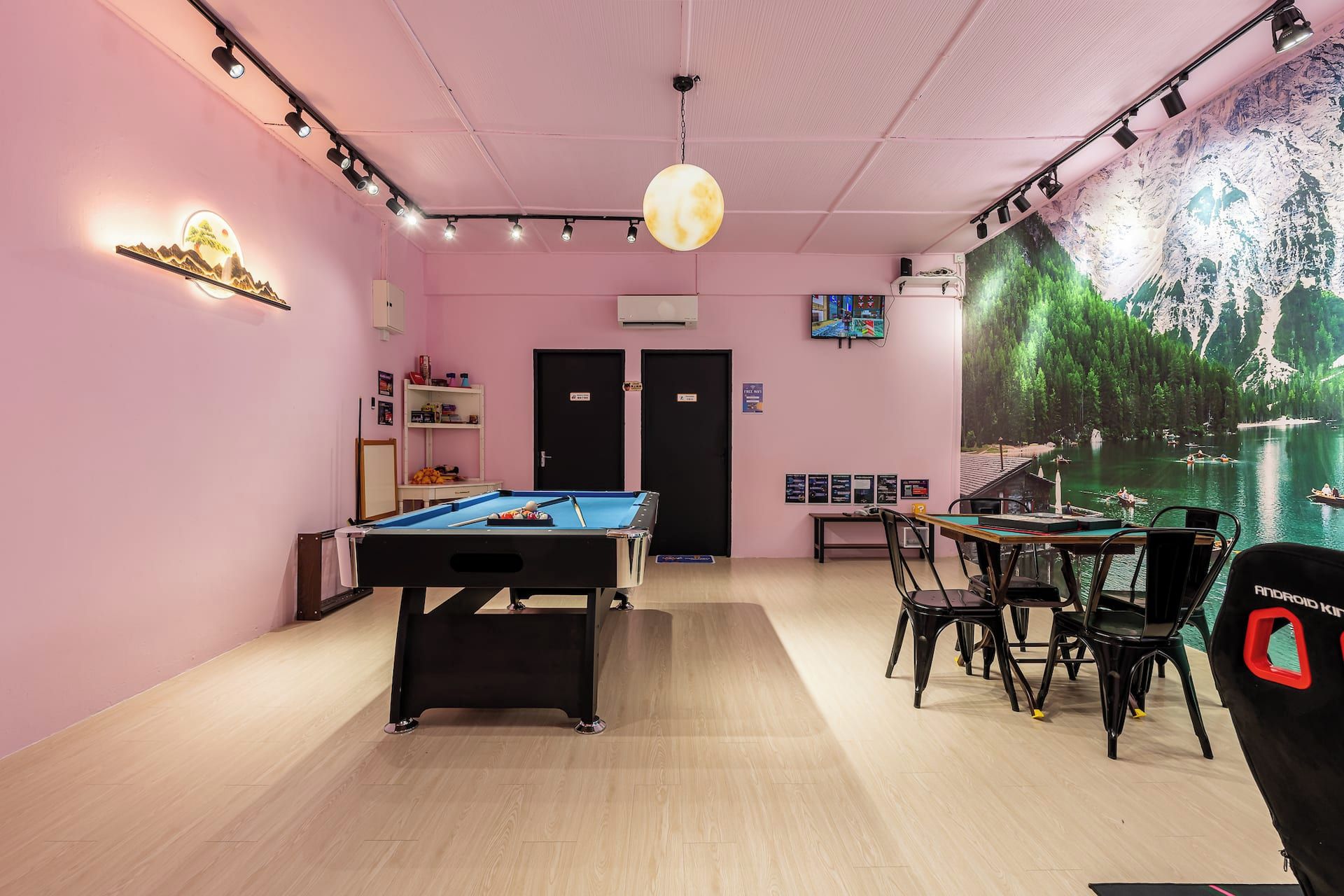 Une pièce équipée d’une table de billard, de chaises, d’une grande fresque murale et d’un luminaire au plafond.