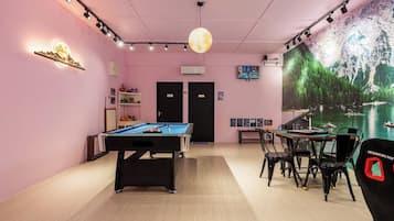 Une pièce équipée d’une table de billard, de chaises, d’une grande fresque murale et d’un luminaire au plafond.