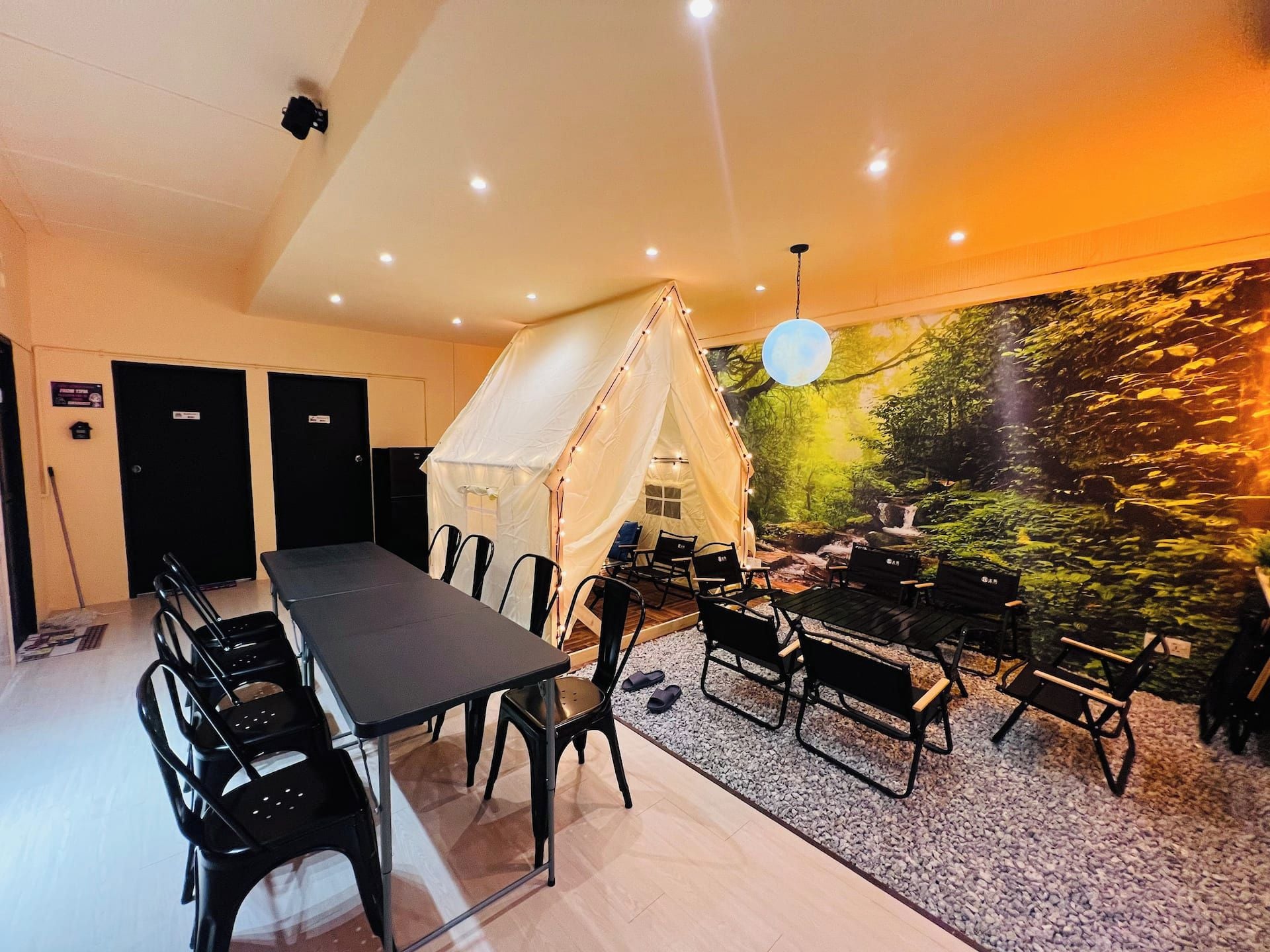 A room with a long table and chairs, a tent-like structure, and a wall mural.