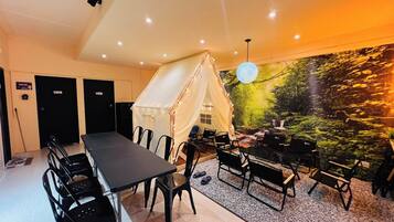 A room with a long table and chairs, a tent-like structure, and a wall mural.