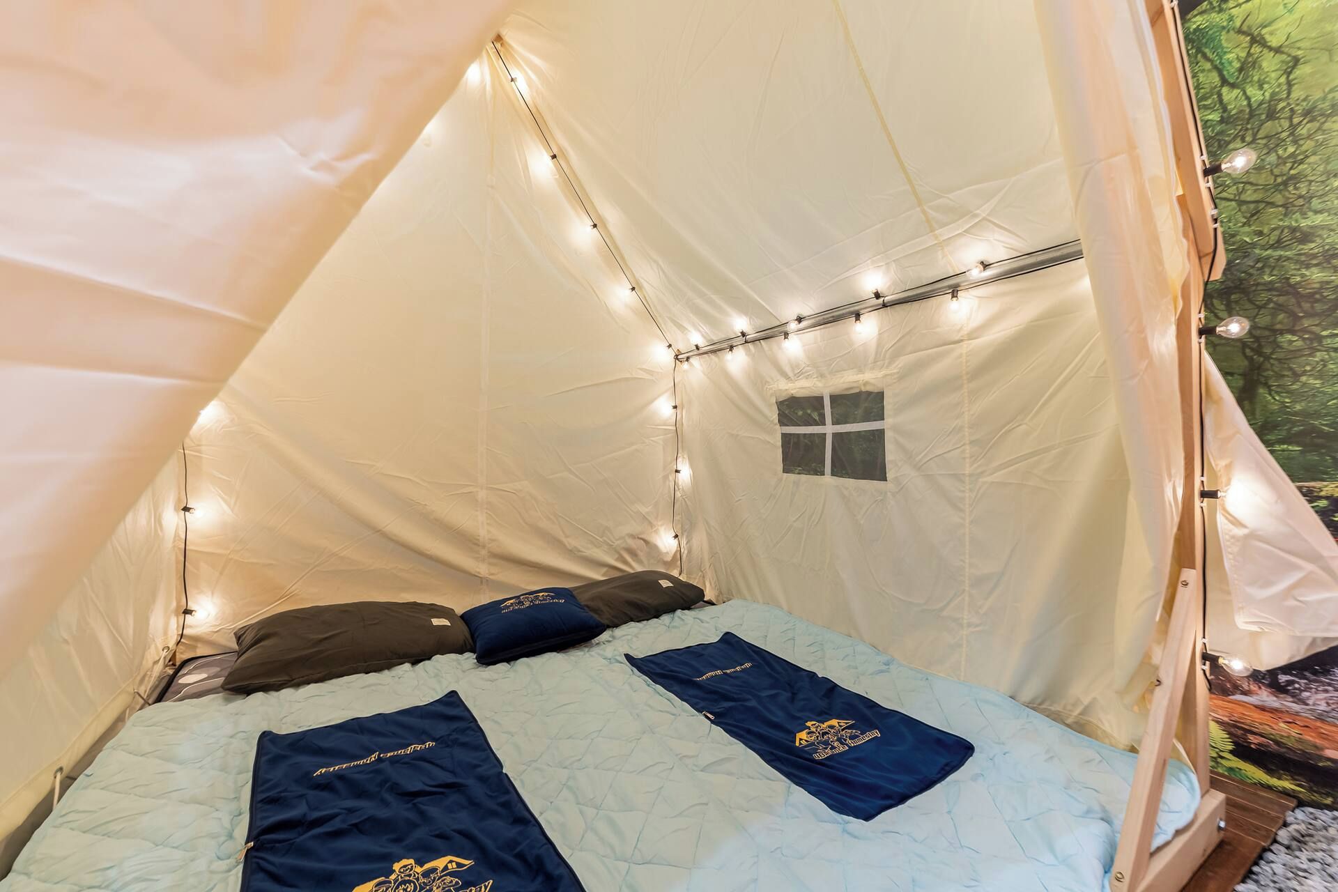 A tent with a bed, string lights, and a small window.