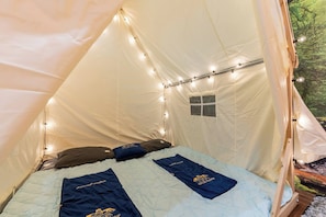 A tent with a bed, string lights, and a small window.
