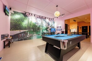 A pool table in a room with a large mural of a lake and mountains.