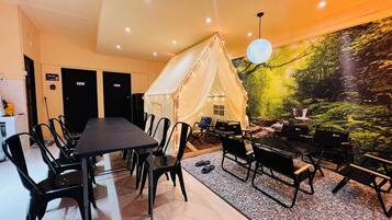 Una habitación con una mesa larga, sillas, una tienda de campaña y un mural con una escena de bosque.