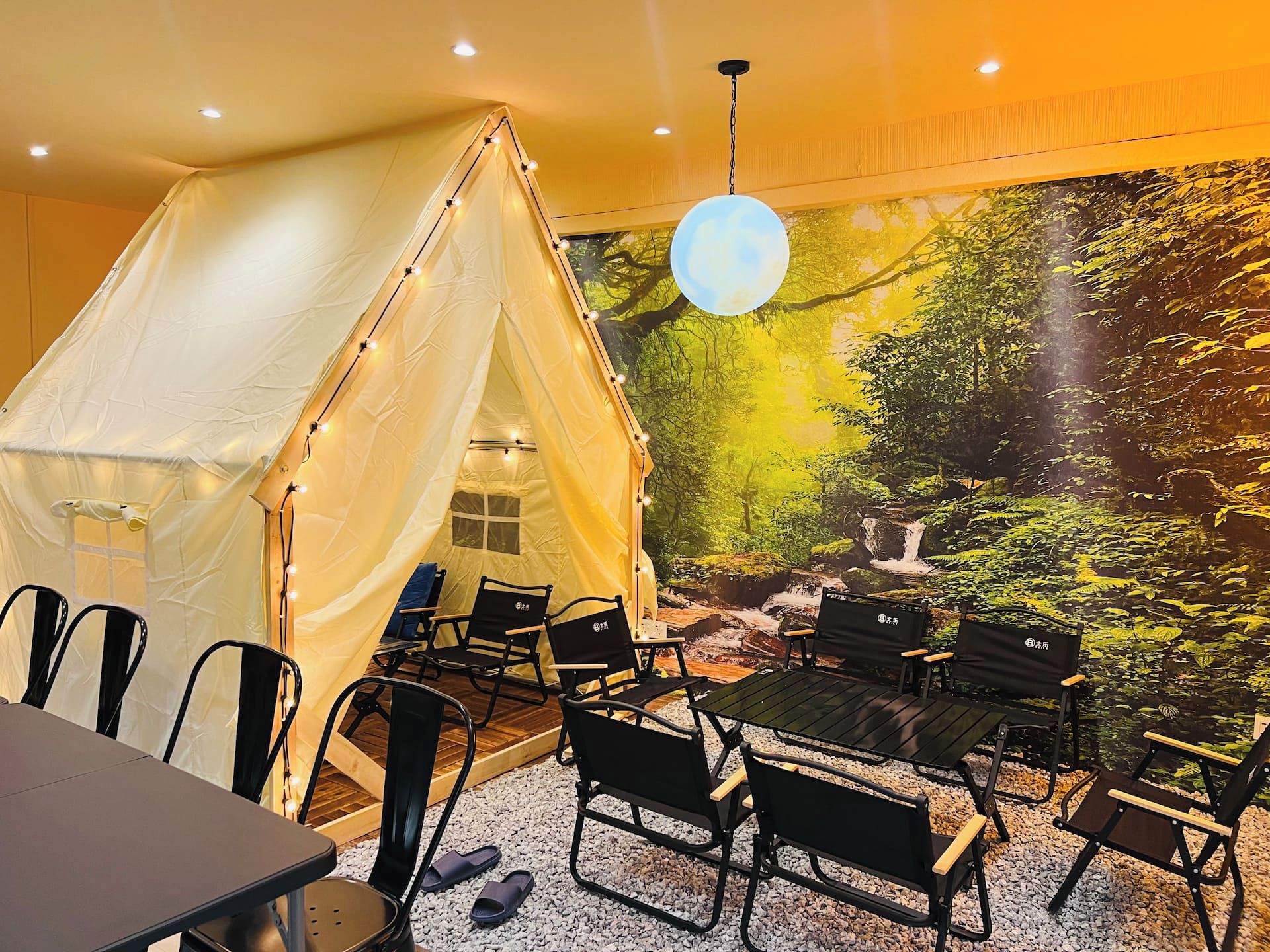 A tented room with a mural of a forest scene, a table, chairs, and a hanging light fixture.