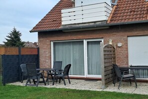 Ein Wohngebäude mit Ziegelaußenwand, einem Ziegeldach und einer überdachten Terrasse mit Gartenmöbeln.