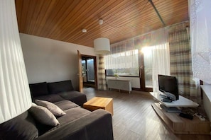 A modern living room with a wooden ceiling, a sofa, a coffee table, a television, and a window with curtains. - Dambach with lake view (Füssen)