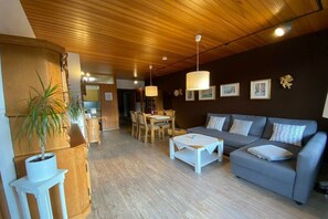 A cozy living area with a sofa, coffee table, and dining table. There is a potted plant and a wooden cabinet. The room has wooden flooring and a dark wall with framed pictures. - Dambach with lake view (Füssen)