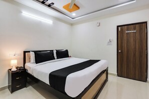 Quarto de hotel com cama, mesa de cabeceira, luminária e porta de madeira.