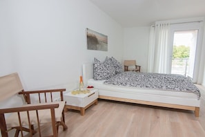 A bedroom with a bed, a nightstand, a chair, a window with curtains, and a painting on the wall. - Holiday apartment with 1 bedroom (Neustadt \/ Pelzerhaken)
