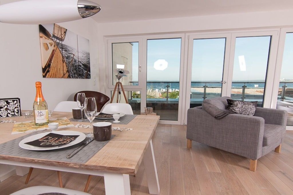 Un coin repas avec une table dressée pour deux personnes, un canapé et une grande fenêtre donnant sur la mer.