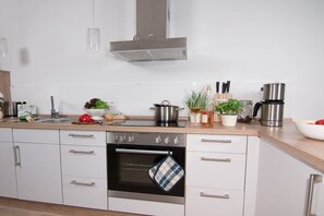 A modern kitchen with white cabinetry, a stainless steel range hood, a built-in oven, and a coffee maker. - Holiday apartment with 1 bedroom (Neustadt \/ Pelzerhaken)