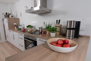 A modern kitchen with white cabinets, a stainless steel range hood, a coffee maker, and a bowl of apples on the counter. - Holiday apartment with 1 bedroom (Neustadt \/ Pelzerhaken)