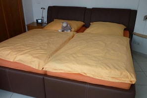 A double bed with a headboard, a nightstand with a lamp, and a stuffed toy on the bed. - Holiday apartment with 1 bedroom (Cuxhaven-Sahlenburg)