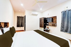 Quarto de hotel com cama, ventoinha no teto, ar condicionado, televisão fixada na parede e janela com cortinas.