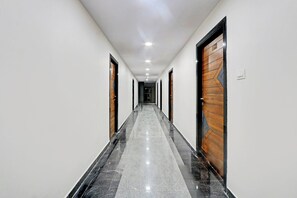 A long, narrow hallway with a polished marble floor, flanked by doors with wooden panels and black frames. - Hotel O RB KOMPALLY (Hyderabad)