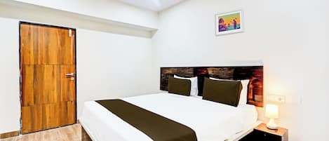 Habitación de hotel con cama, mesita de noche, lámpara de pared, ventilador de techo y puerta de madera.