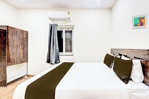 Quarto de hotel com cama, guarda-roupa, ar condicionado, janela com cortinas e uma obra de arte na parede.
