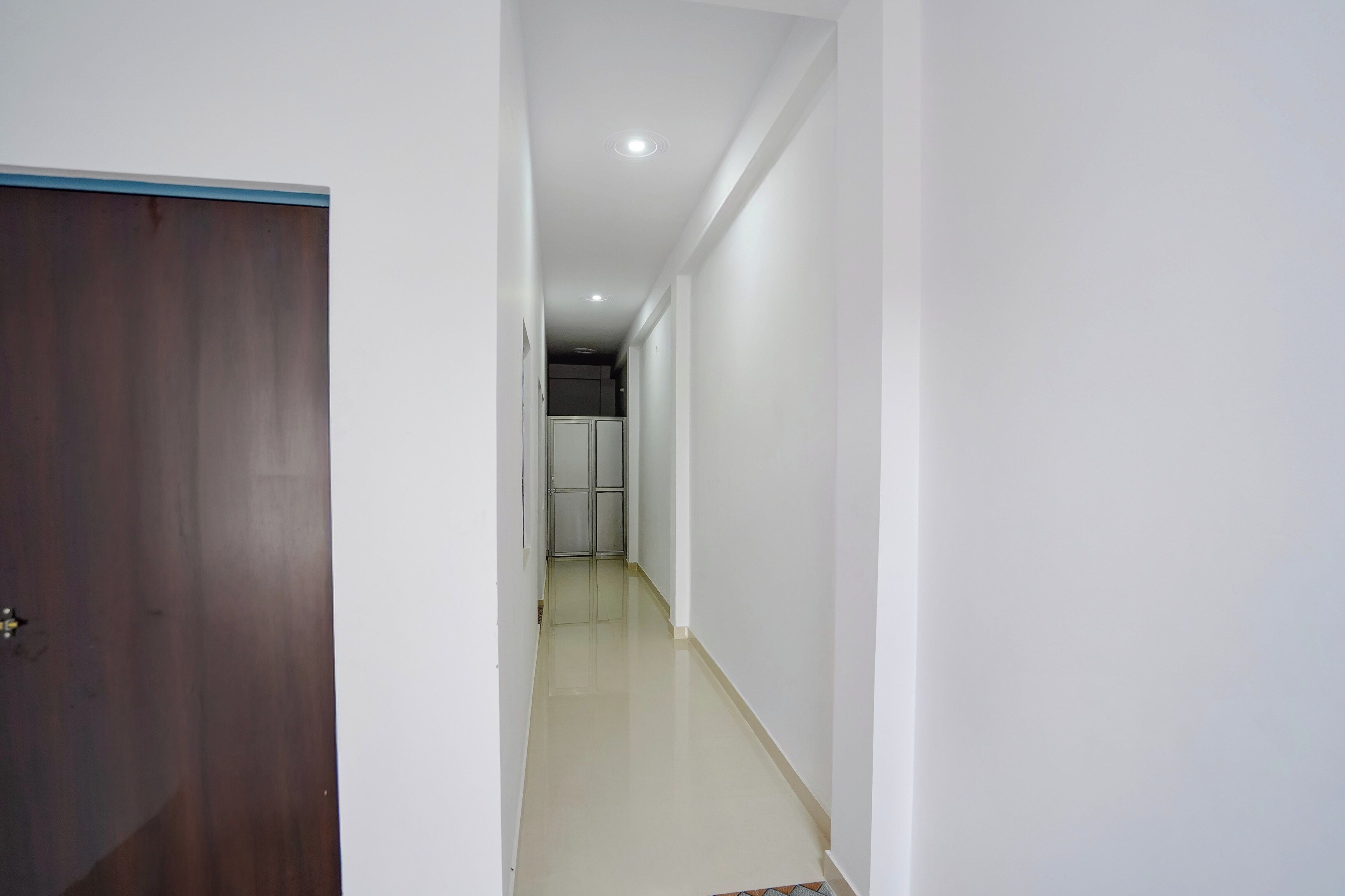 A narrow hallway with a wooden door on the left, a tiled floor, and a white wall.