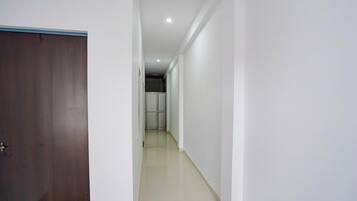 A narrow hallway with a wooden door on the left, a tiled floor, and a white wall.