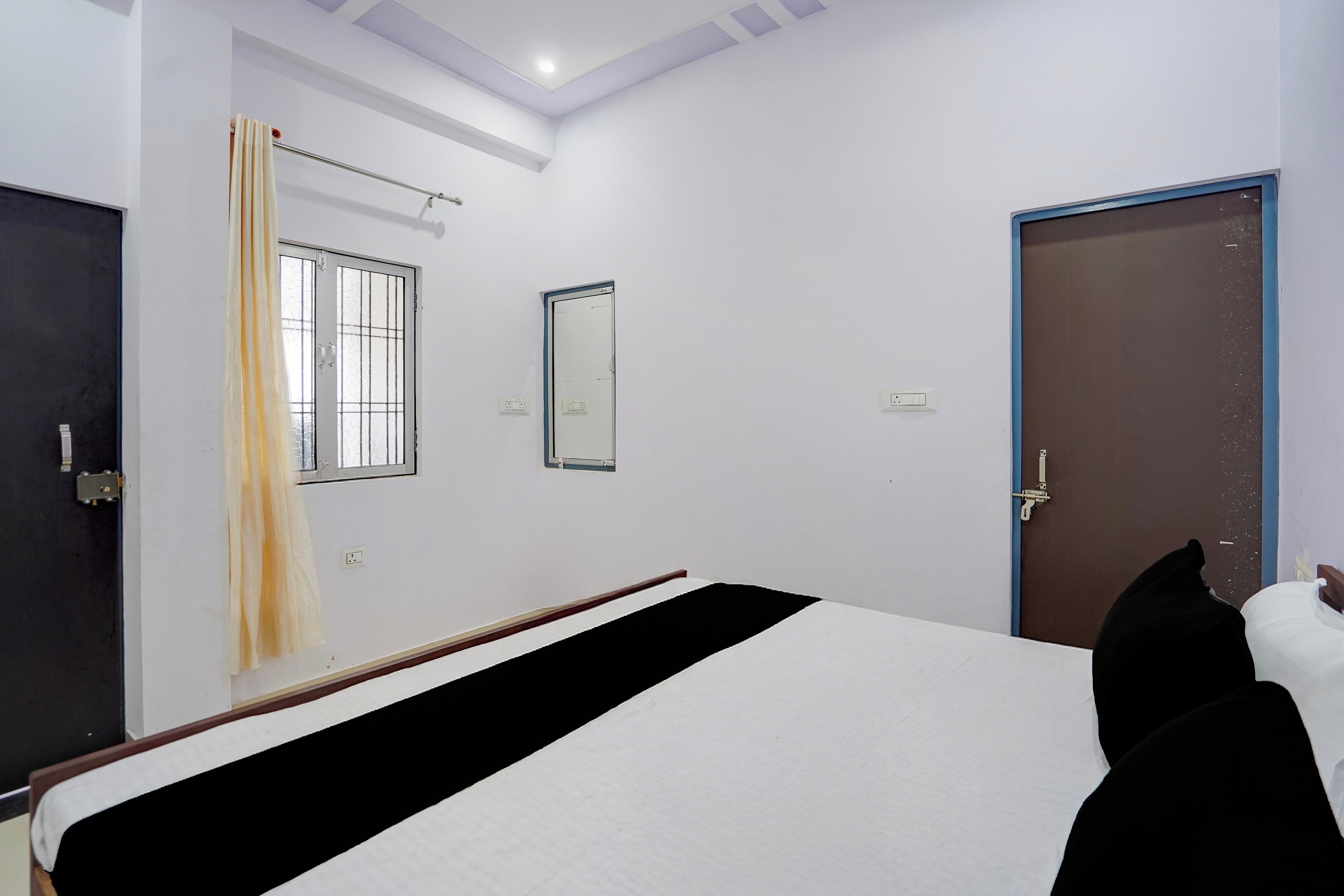 A hotel room with a bed, a window, a door, and a mirror.