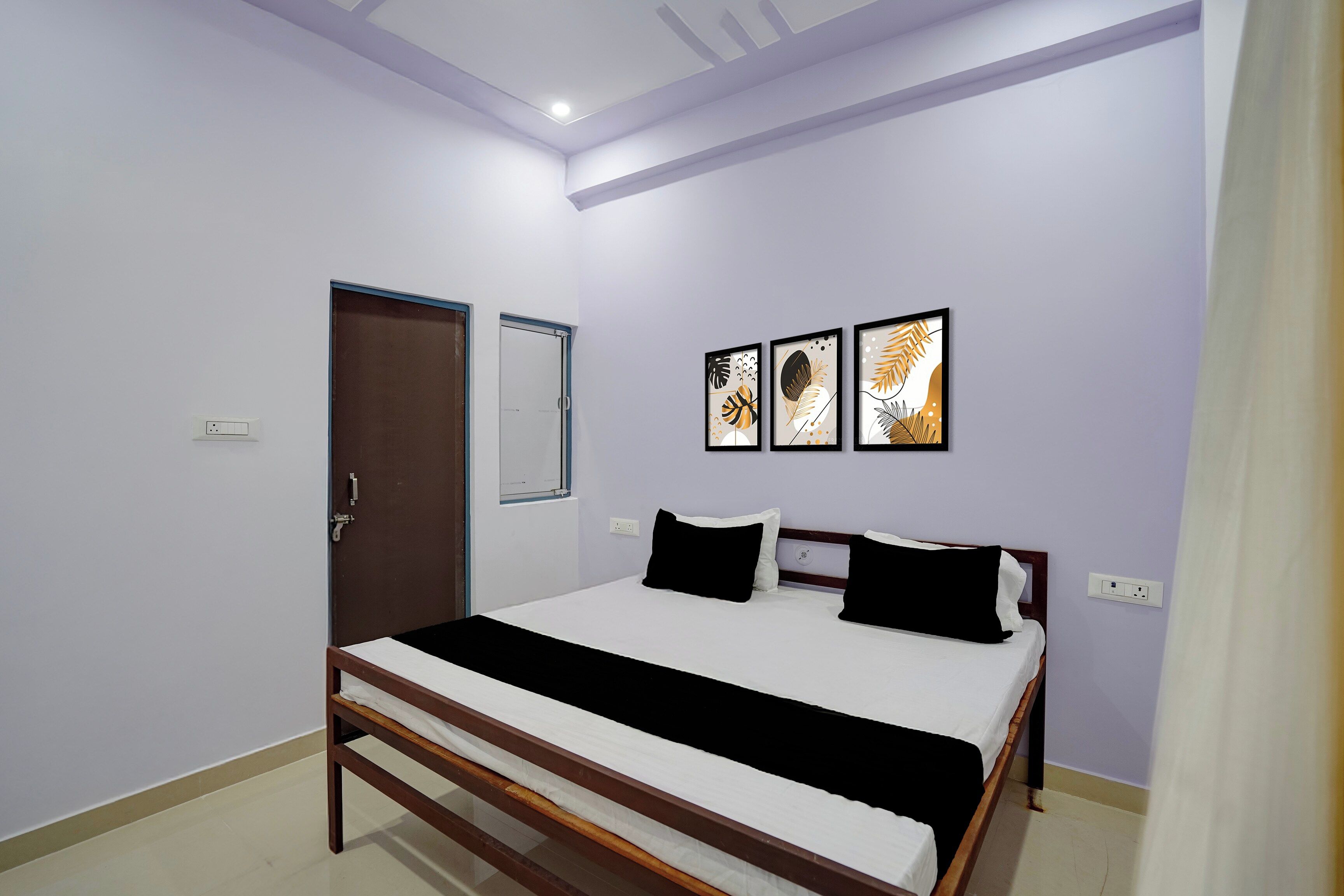 A bedroom with a bed, a door, and three framed artworks on the wall.