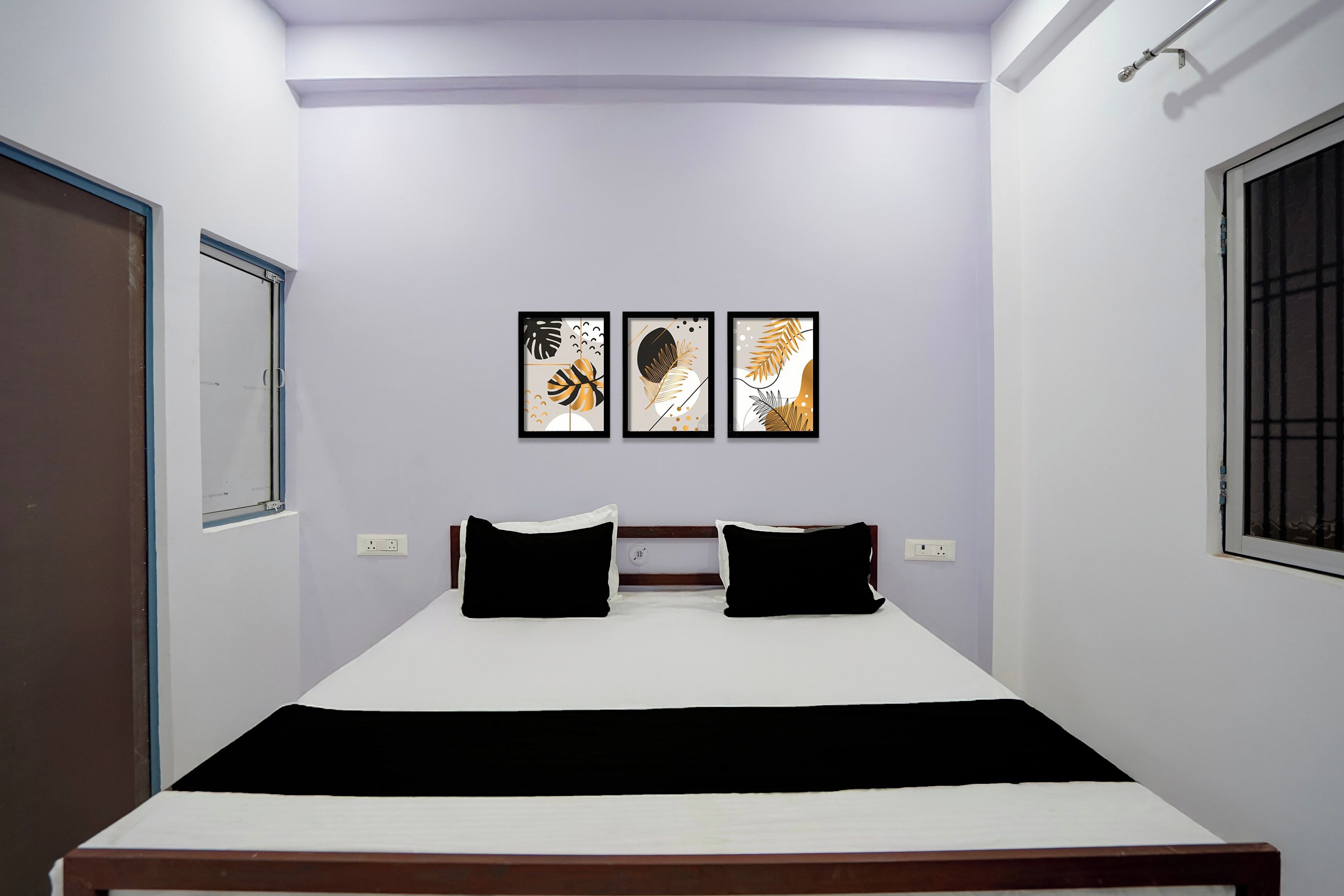 A bedroom with a bed, two pillows, a nightstand, and three framed artworks on the wall.