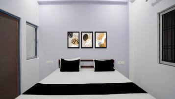 A bedroom with a bed, two pillows, a nightstand, and three framed artworks on the wall.