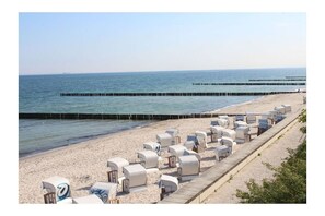 En strand med rækker af hvide liggestole og parasoller, en træpromenade og en mole, der strækker sig ud i vandet.