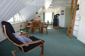 A room with a sloped ceiling, a dining area with wooden furniture, a chair with a cushion, and a small table with a bottle and glass. - Holiday apartment with 1 bedroom (Pruchten)