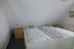 A bedroom with two single beds, a nightstand with a lamp, a radiator, and a small drawer. - Holiday apartment with 1 bedroom (Pruchten)