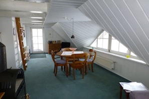 Une pièce avec un plafond en pente, une table à manger avec des chaises, un radiateur et une fenêtre.