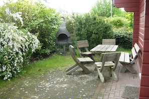 An outdoor patio with a stone-tiled floor, wooden picnic table and benches, and a stone oven. - Holiday home in Zingst with barbecue (Zingst)